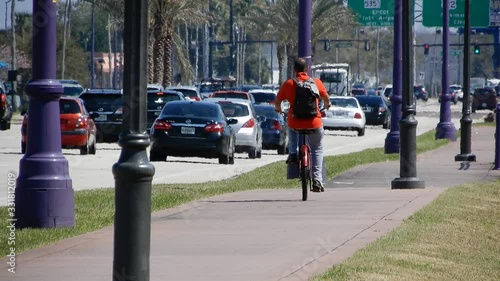 Cyclist Cycling Down Sidewalk In Hot Summer Heat With Lots Of Traffic And Heat Waves With Disney Epcot Sign In Distance photo