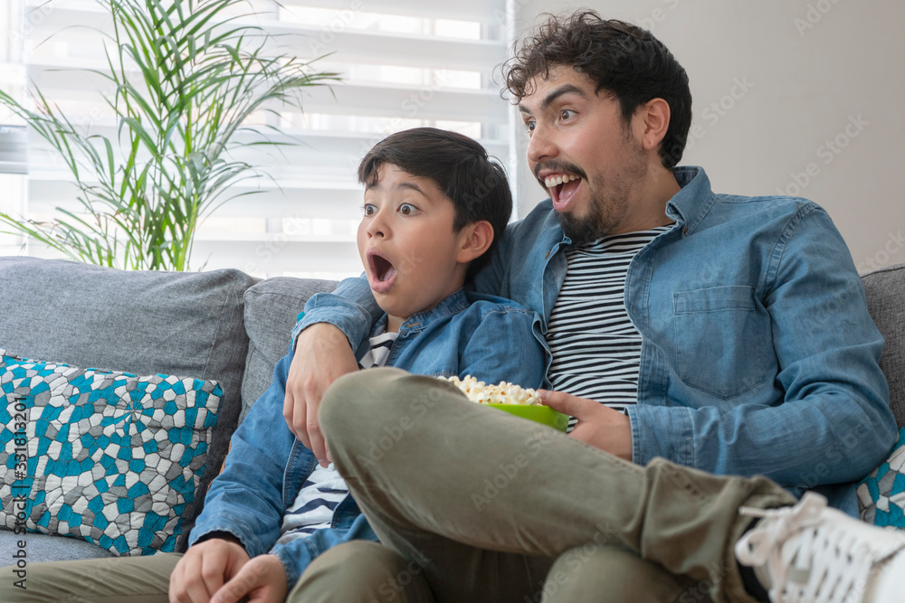 Fototapeta premium Padre e hijo asombrados viendo la tv con palomitas