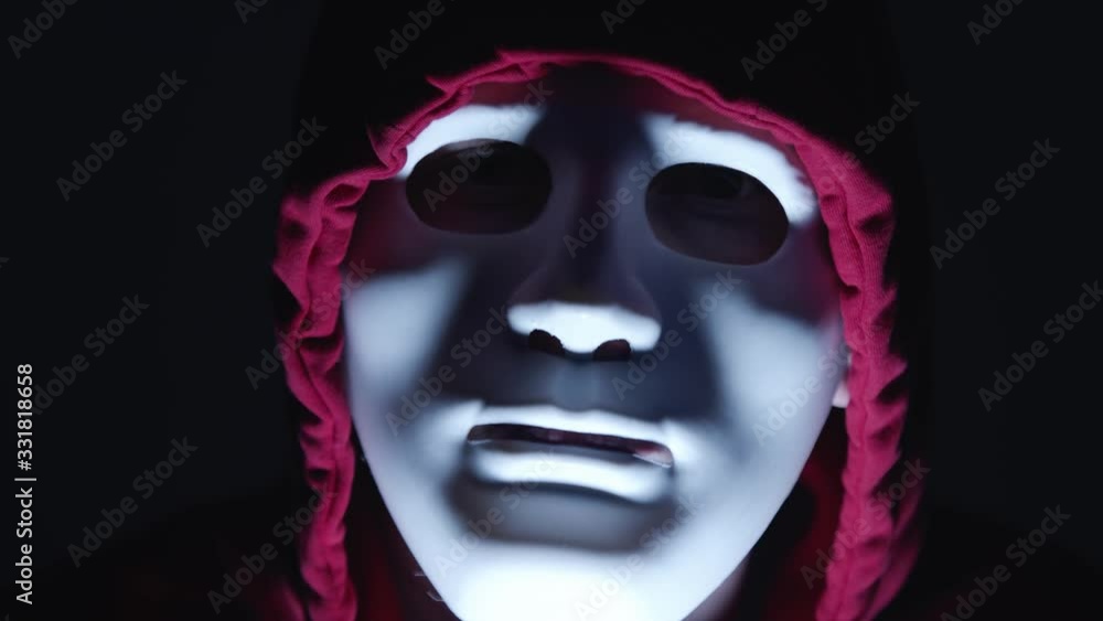 scary creepy man with white mask and reed hoodie. Head shot. Thief in the action scary creepy man with white mask and reed hoodie. Head shot. Thief in the action