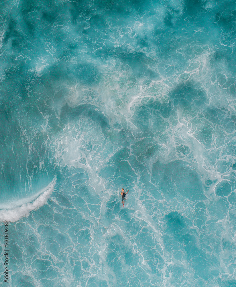 Surfing paddling in waves view from drone