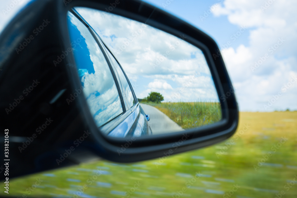 Side rear-view mirror car reflection of a countryside road
