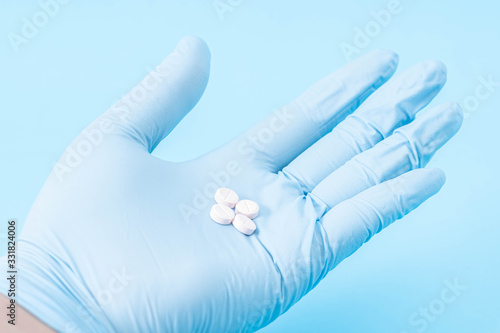 Hand with blue gloves holding different pills on blue background