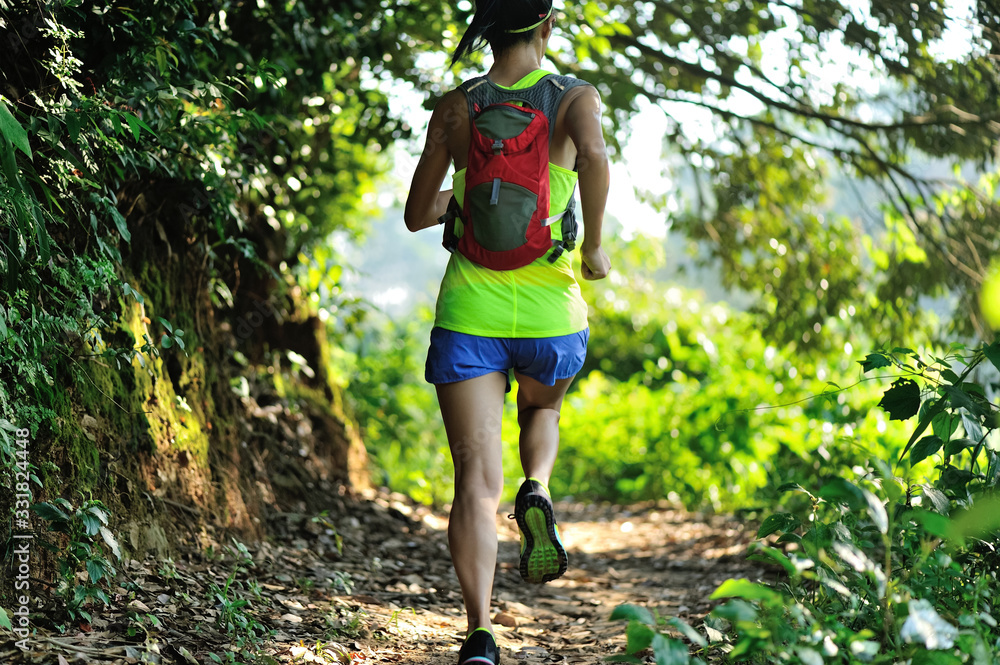 Fototapeta premium Young woman trail runner running in sunrise tropical forest