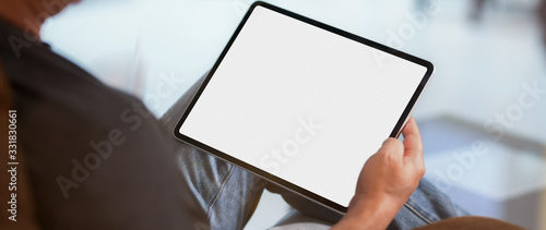 Cropped shot of a man sitting at living room and using blank screen  tablet