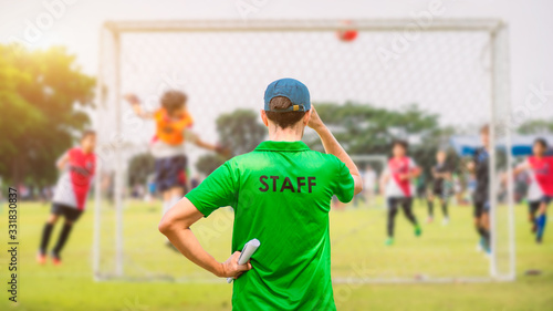 Staff coaches who stand to watch athletes compete on the side of the field. Rear view.