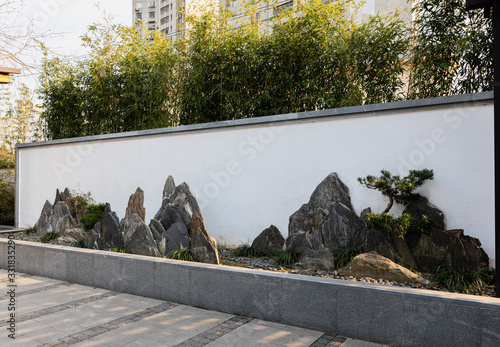 Photography Traditional Chinese landscape painting consisting of rock slices, trees & grass in front of a white wall at public Jiangwan Park in historical, old town Jiangwanzhen, Hongkou, Shanghai, China