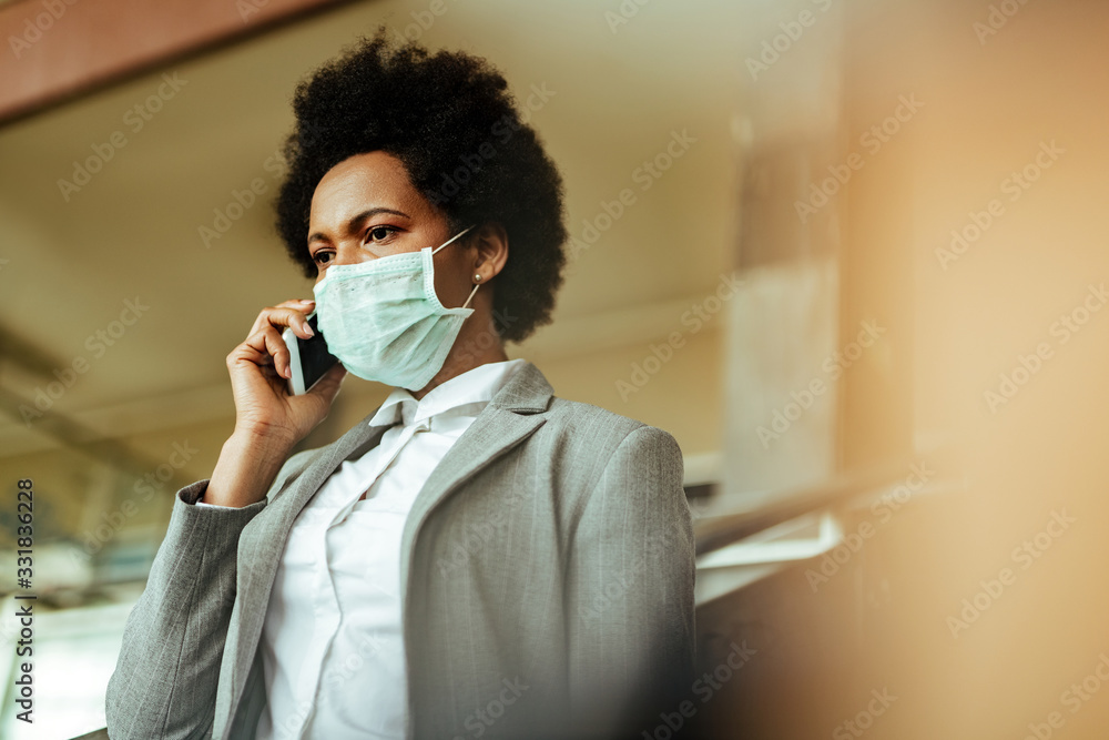 Black businesswoman wearing face mask while making a phone call at the airport.