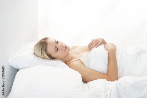 Young woman lying in the bed. Beautiful blond sleeping girl. Morning in the bedroom, daylight from the window. Health and rest.