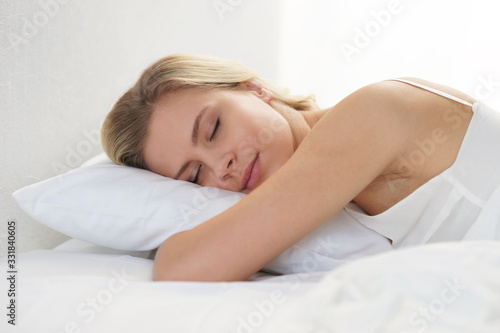 Young woman lying in the bed. Beautiful blond sleeping girl. Morning in the bedroom, daylight from the window. Health and rest.