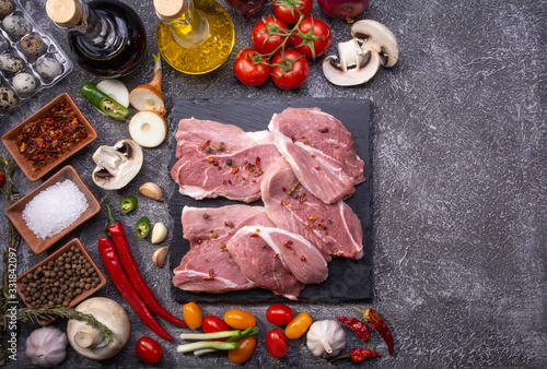 Pork cuts for steaks, fresh vegetables, spices close-up on a textured background