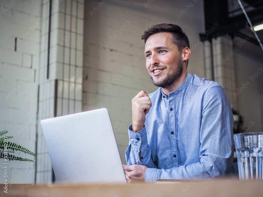 happy smiling remote online working man having one hand up with laptop and notebook in casual outfit with sitting in an coworking or home office at a work desk explaining something happy smiling remote online working man having one hand up with laptop and notebook in casual outfit with sitting in an coworking or home office at a work desk explaining something