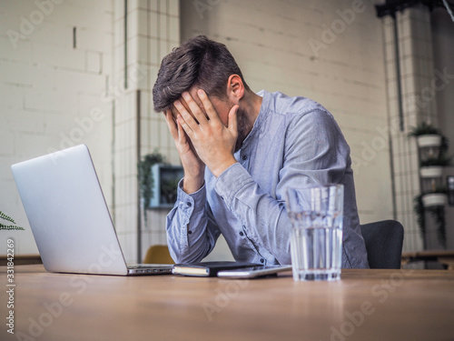 worried and disappointed remote online working man in casual outfit with laptop sitting in an coworking / home office at a work desk photo