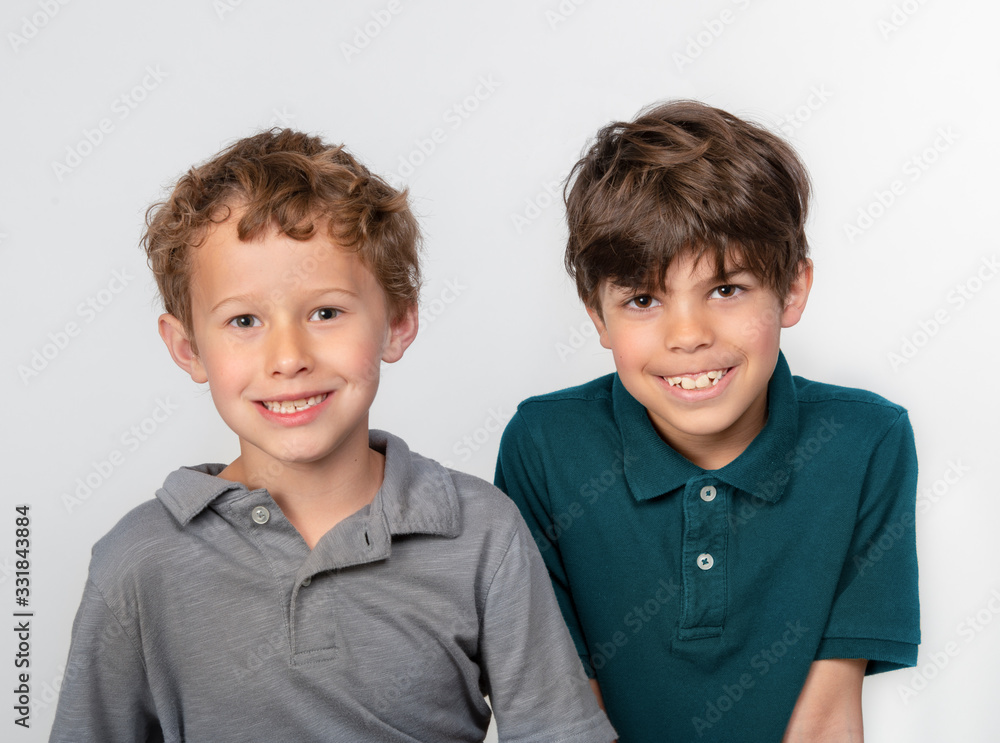 Obraz premium Two smiling little boys in polo shirts sitting side by side isolated on white background