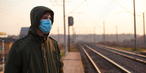guy in a disposable medical mask standing at the train station on the sunset. quarantine respiratory viral disease epidemic coronavirus flu Public transport stops due to the outbreak of Covid-19