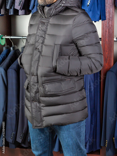 A young man is standing in a long jacket at a clothing store with his hands in his pockets