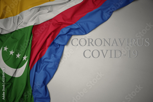 waving national flag of comoros on a gray background with text coronavirus covid-19 . concept.