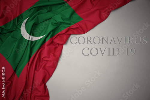 waving national flag of maldives on a gray background with text coronavirus covid-19 . concept.