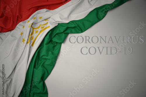 waving national flag of tajikistan on a gray background with text coronavirus covid-19 . concept.