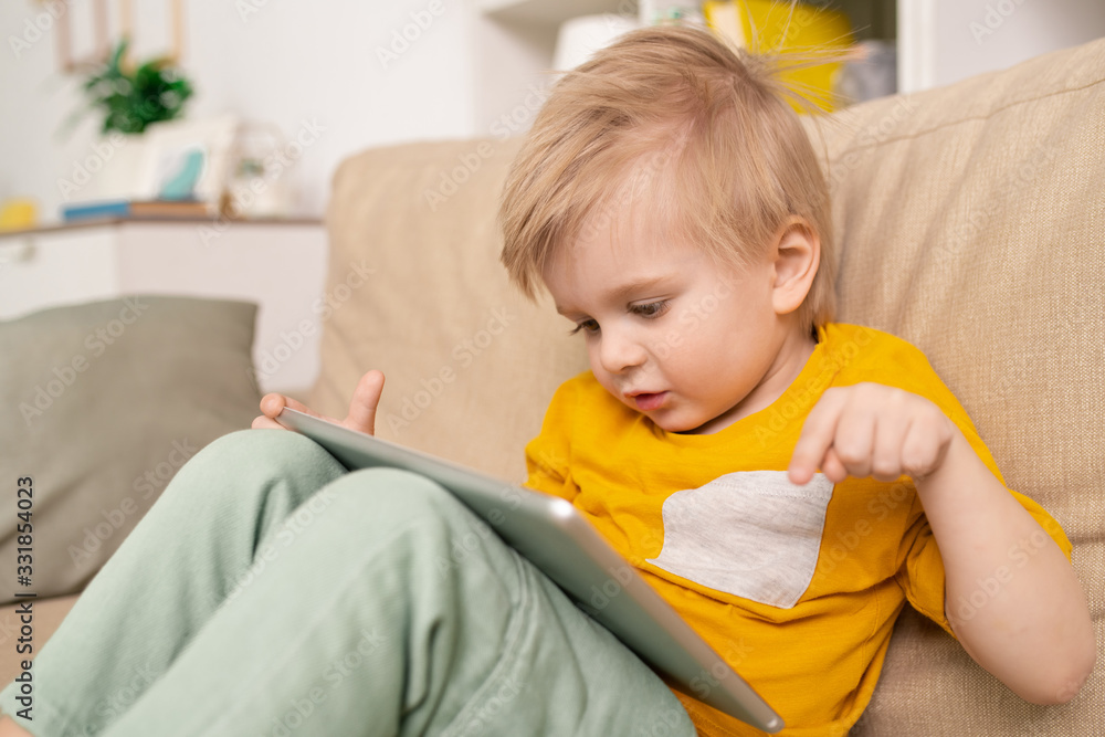 Close-up of cute boy sitting on sofa and talking to parent via telecommunication app on tablet in living room Close-up of cute boy sitting on sofa and talking to parent via telecommunication app on tablet in living room