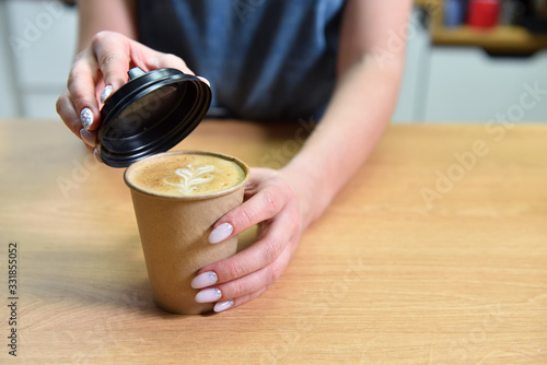 Barista making coffee and closes the paper cup with a lid, hands closeup. Coffee shop small business concept.