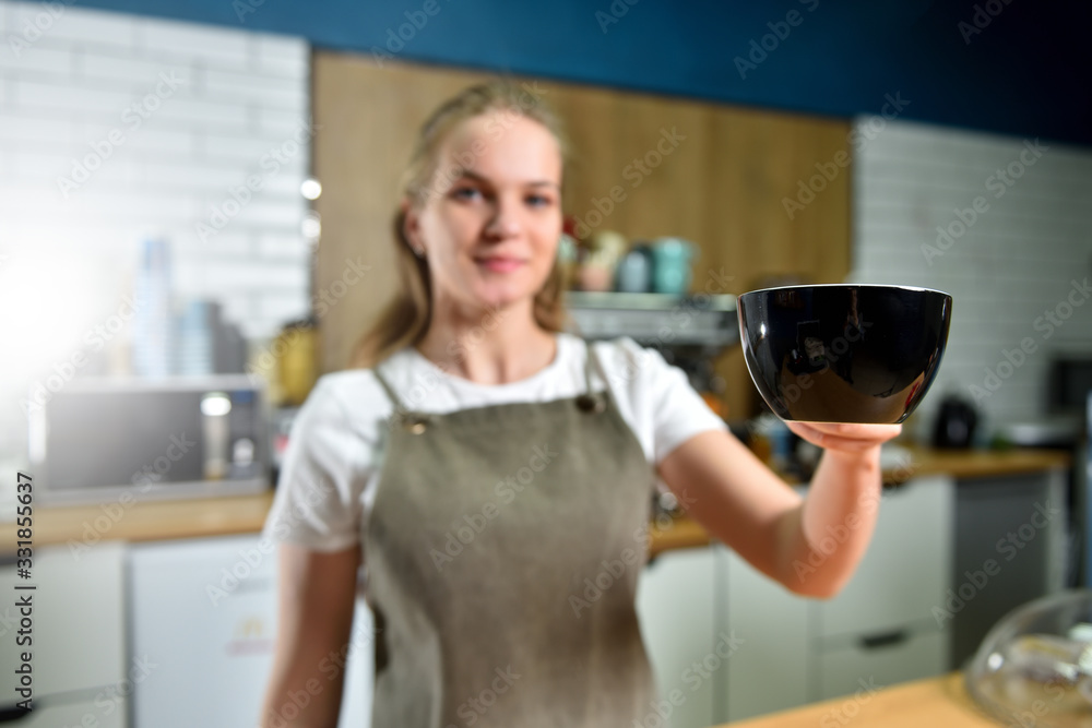 A young barista girl offers a large cup with coffee. Small business concept.