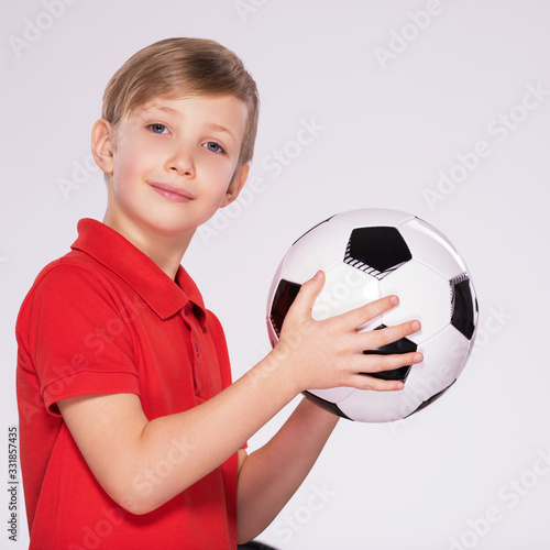 Pretty 8 years old kid in a red t-shirt with a soccer ball in hand. Photo of a boy in sportswear holding soccer ball, posing at studio. White child holds a soccer ball.