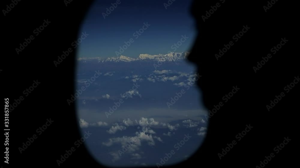 A close view of a persons silhouette looking out of planes window. View of sky and clouds out of an airplane window. A close view of a persons silhouette looking out of planes window. View of sky and clouds out of an airplane window.