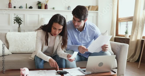 Young couple calculating bills, taxes and expenses, counting mortgage rate making savings concept. Millennial husband and wife considering taking bank loan, investing money. Family financial economy. photo