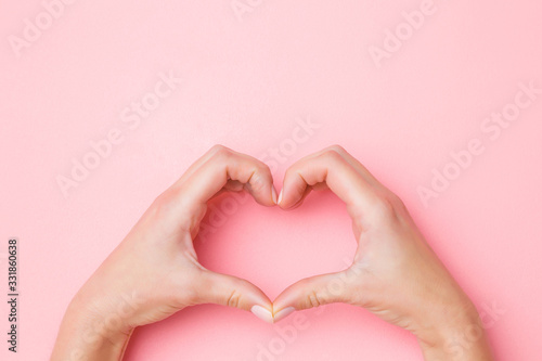 Canvastavla Heart shape created from young woman hands on pastel pink table background