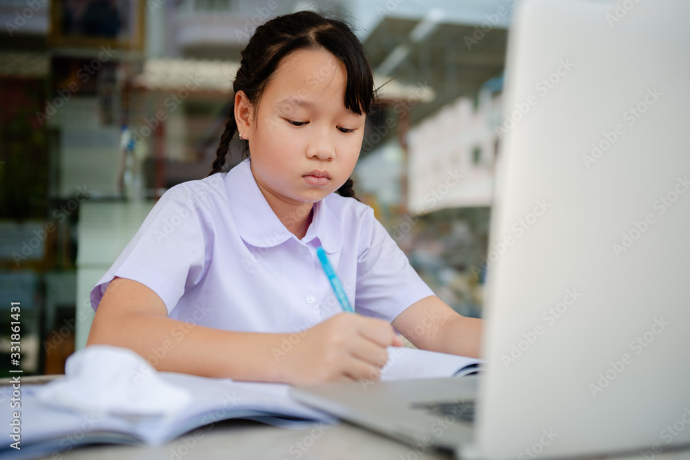 social distancing concept, Junior Primary school girl Do homework at home with laptop. the school is closed during an outbreak of the Coronavirus Covid-19 and Dust PM2.5 in Bangkok Thailand asia social distancing concept, Junior Primary school girl Do homework at home with laptop. the school is closed during an outbreak of the Coronavirus Covid-19 and Dust PM2.5 in Bangkok Thailand asia