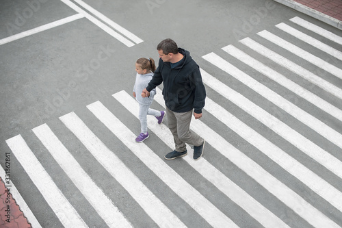 Man and child on a zebra crossing trespassing by crossing the street. In the summer on the street kid girl with her father in fashion clothes cross the road. From top view. Traffic rules for children