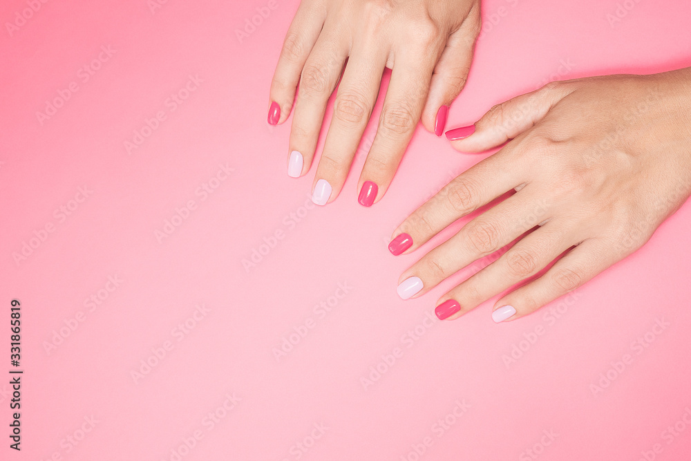 Closeup top view photography of two beautiful female hands isolated on pastel pink background with empty space for text. Fingernails with modern trendy assymetric two colors design of manicure.