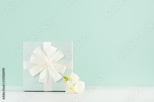 Beautiful fresh spring festive background with elegant standing gift box, white flowers freesia in green mint menthe interior on white wood board.