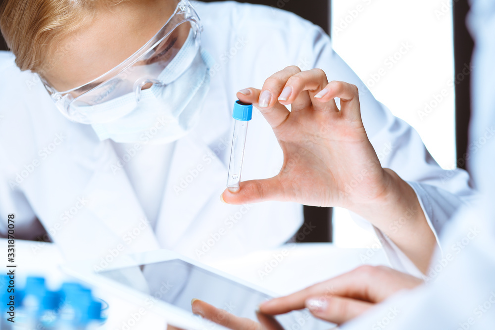 Coronavirus pandemic. Professional female scientist in protective eyeglasses researching tube with reagents in laboratory. Concepts of medicine and virus protection Coronavirus pandemic. Professional female scientist in protective eyeglasses researching tube with reagents in laboratory. Concepts of medicine and virus protection
