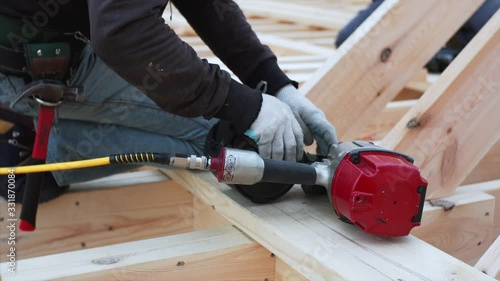 Builder is loading pneumaic nail gun with nails. Wooden frame house building site