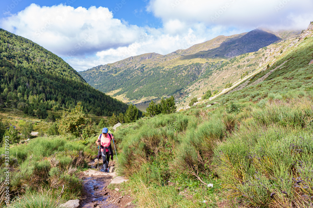 View of lady hiker, going up to the lakes of Juclar with the Incles Valley in the background. Soldeu, Andorra