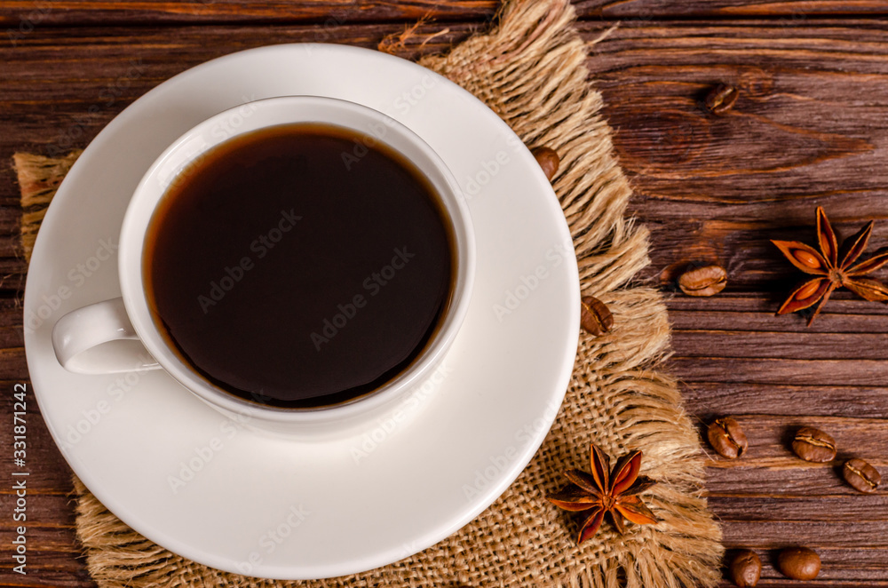 Cup of black aromatic coffee in a white cup with anise stars and cinnamon sticks on a wooden background. Cup of black aromatic coffee in a white cup with anise stars and cinnamon sticks on a wooden background.