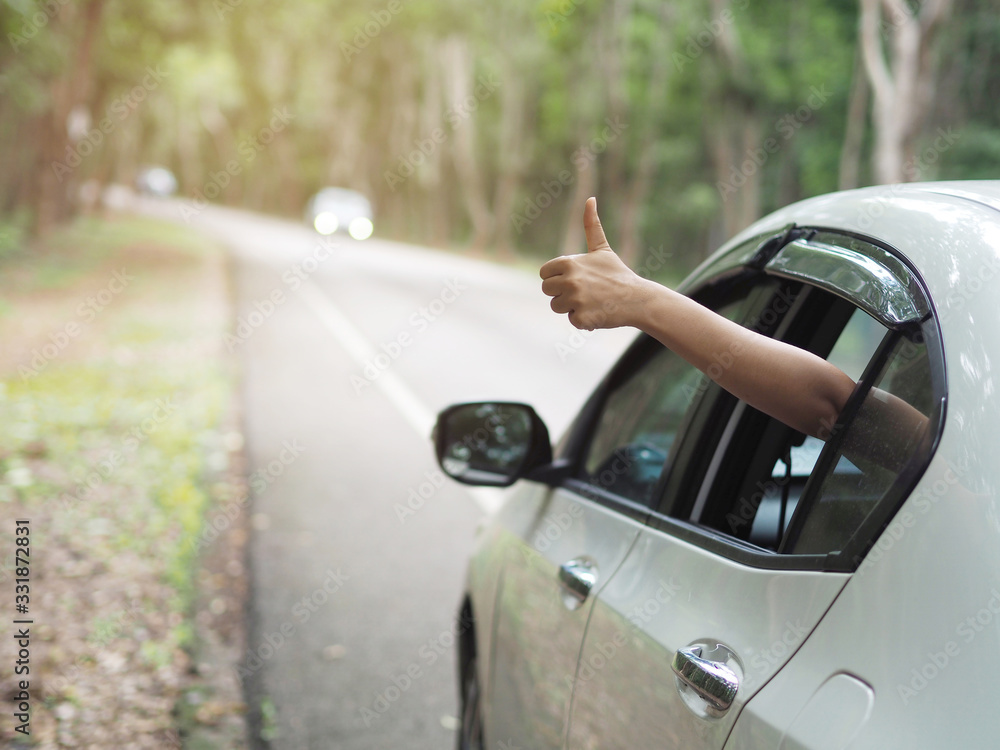 asian woman hold her hand out from the window car and show thumps up sign and she happy ,enjoy road trip. use for travel insurance background concept.