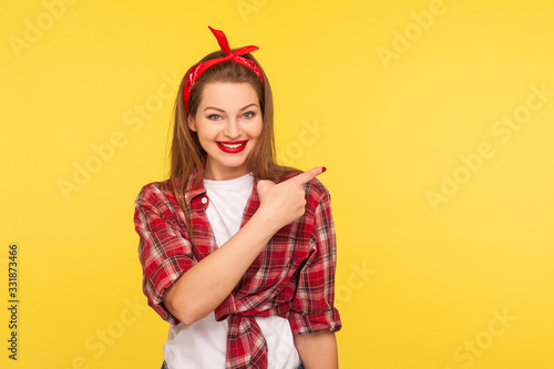 Look, advertisement! Portrait of optimistic attractive pinup girl smiling and pointing to empty wall, showing copy space