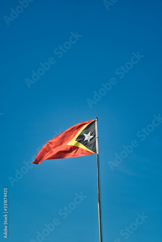 Timor Leste ( East Timor ) flag waving on the mastg. Blue background sky. Youngest country in southeast Asia.
