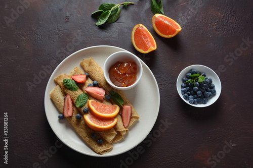 Sweet pancakes wrapped with fresh mint, strawberries, blueberries, oranges and jam. Healthy breakfast concept
