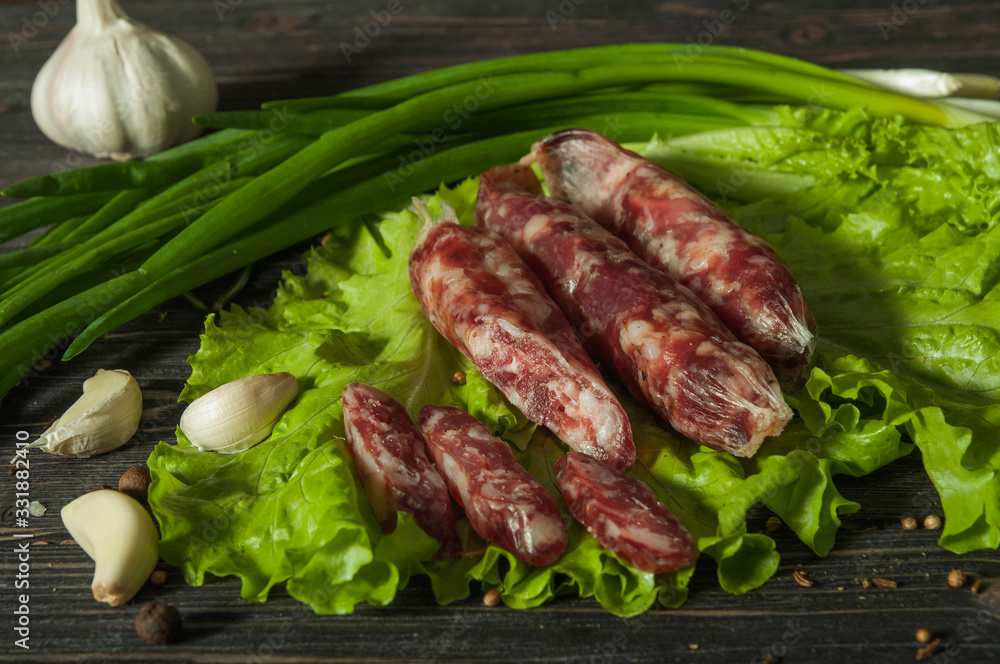 Sausage with garlic and herbs. On the brown table is a sausage with greens. Delicious country food. Delicious sausage with herbs and garlic. Sausage with garlic and herbs. On the brown table is a sausage with greens. Delicious country food. Delicious sausage with herbs and garlic.