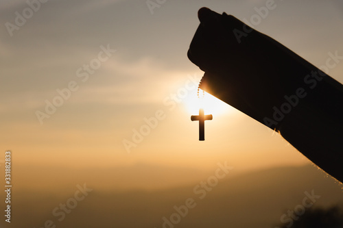human hands praying to the GOD while holding a crucifix symbol with bright sunbeam.