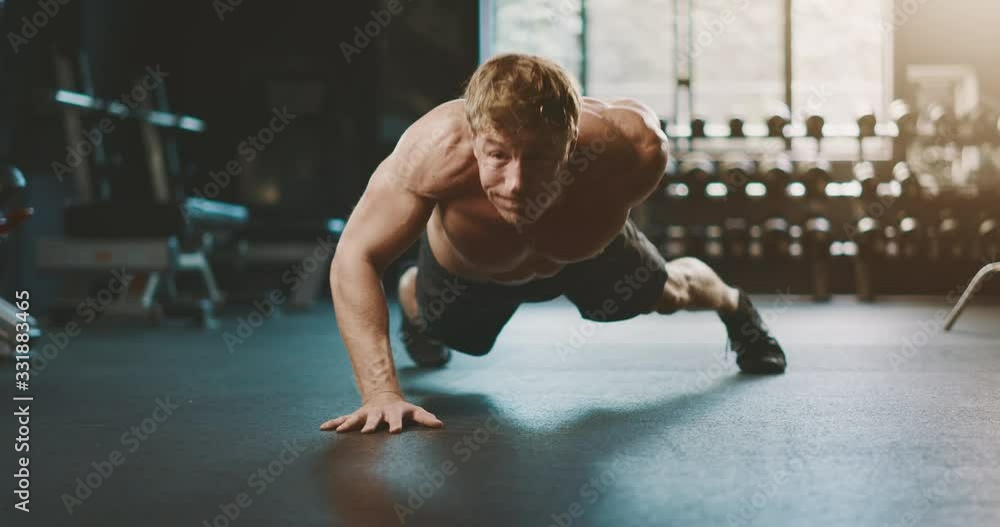 Strong muscular man working out in the gym doing one armed push ups with intense emotions, determined fitness man focused on getting stronger Strong muscular man working out in the gym doing one armed push ups with intense emotions, determined fitness man focused on getting stronger
