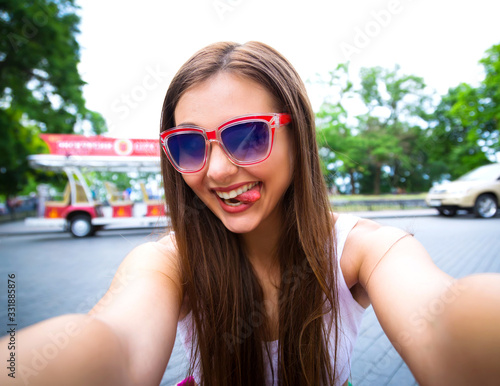 Beautiful hipster girl taking selfie sending kisses.Portrait of a beautiful young tourist woman on holiday, using her smartphone to take a selfie photo of herself during a sunny day. 