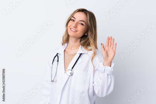 Young woman over isolated white background wearing a doctor gown and saluting