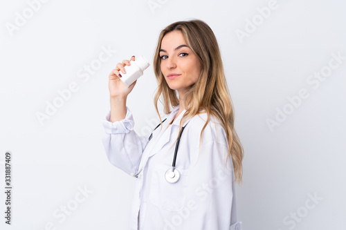 Young woman over isolated white background wearing a doctor gown and holding pills