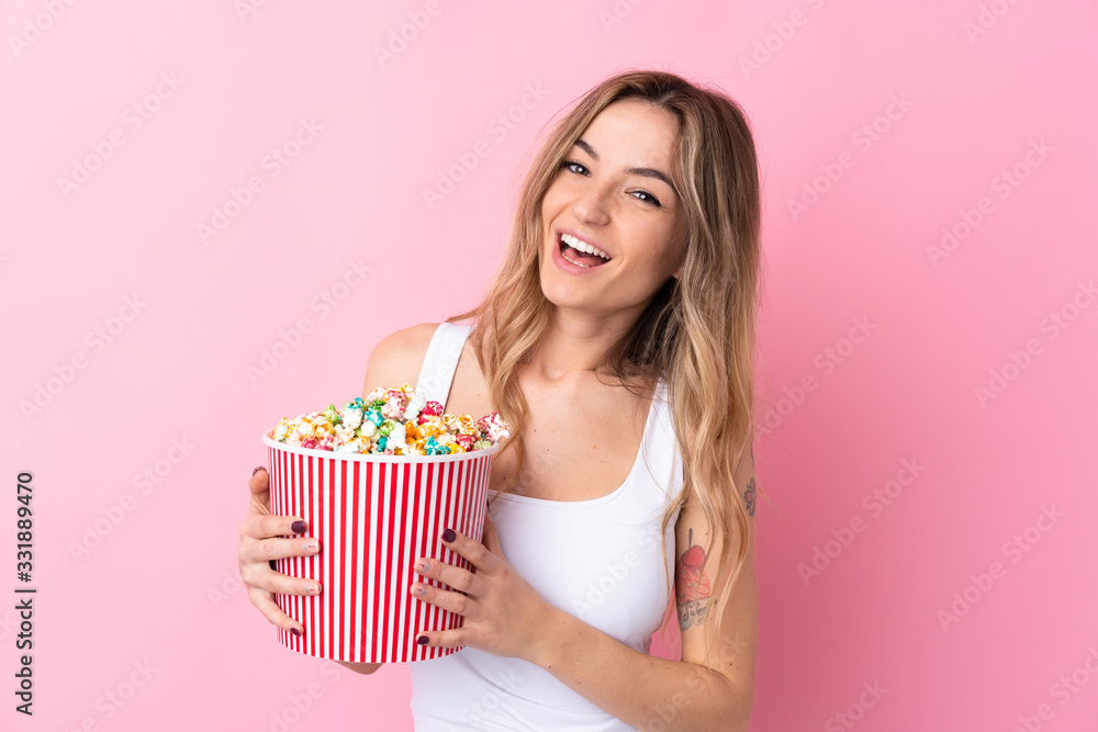 Young woman over isolated pink background holding a big bucket of popcorns Young woman over isolated pink background holding a big bucket of popcorns