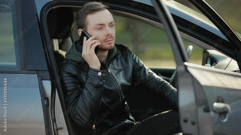 Stylish man in leather jacket talking by smartphone in a car Stylish man in leather jacket talking by smartphone in a car