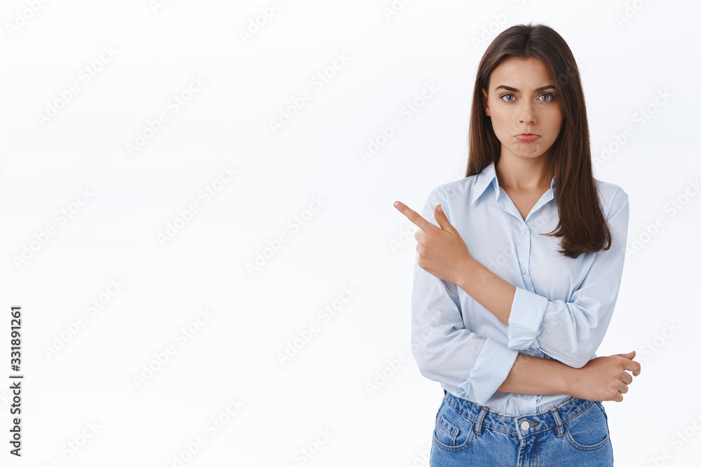 Offended sulking cute caucasian girl in blue blouse pointing finger left, pouting and looking camera with insulted whining or complaining expression, standing disappointed and displeased Offended sulking cute caucasian girl in blue blouse pointing finger left, pouting and looking camera with insulted whining or complaining expression, standing disappointed and displeased